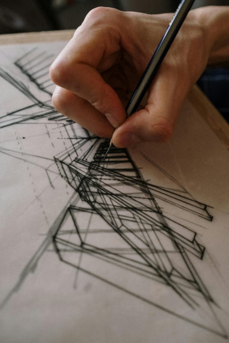 Detailed view of a hand drawing an abstract geometric design with pencil on paper.